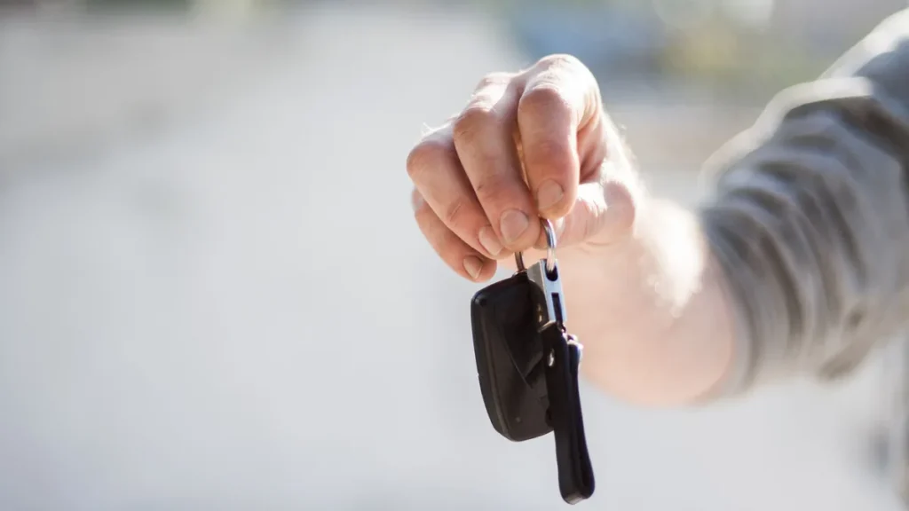 Mão estendida segurando a chave de um carro, com o fundo desfocado